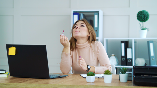Pretty girl applying lip gloss at workplace - Záběry, video