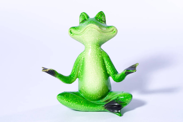 Close up of green frog figure doing yoga meditation, isolated on white - 写真・画像