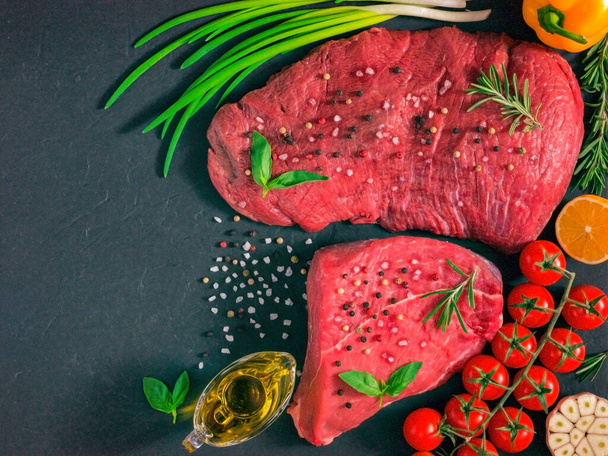 Raw meat. Raw beef steak on dark board with fresh herbs, vegetables, seasonings and spices. Top view or flat lay. Copy space - Fotó, kép