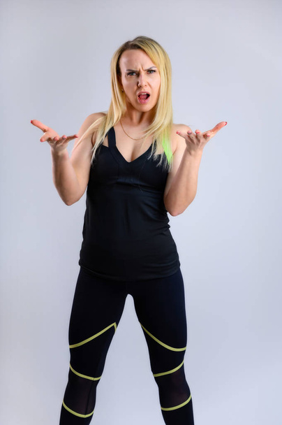 The concept of effective fitness. Full-length vertical photo of a pretty slender blonde woman athlete in a sports suit on a white background. Standing in different poses with emotions and a smile. - Foto, imagen