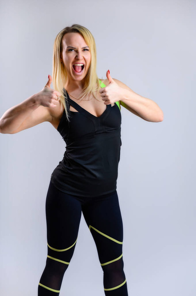 Full-length vertical photo of a pretty slender blonde woman athlete in a sports suit on a white background. The concept of effective fitness. Standing in different poses with emotions and a smile. - Fotografie, Obrázek