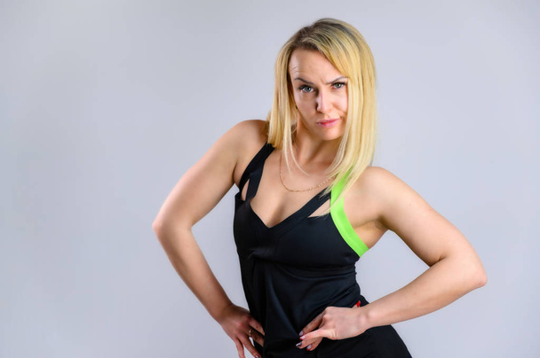 Photo of a pretty slim blonde woman athlete in a tracksuit on a white background. The concept of effective fitness. Standing in different poses with emotions and a smile. - Foto, Bild