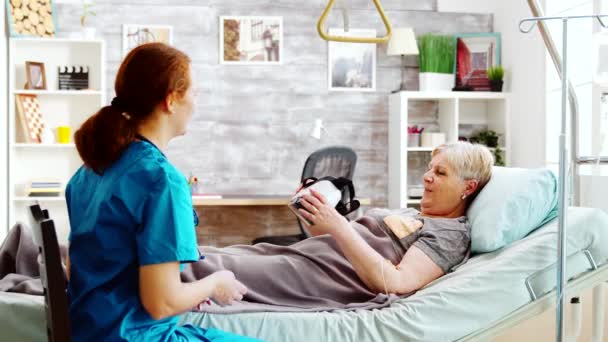 Женщина-медсестра в доме престарелых дает старушке-инвалиду гарнитуру VR - Кадры, видео