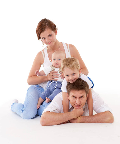 Young parents with sweet  children sit on a white background. Happy family. Six month and four years. - Fotoğraf, Görsel