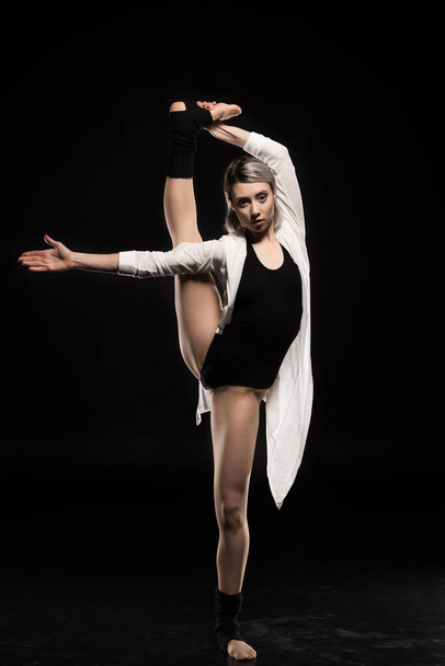 woman in bodysuit stretching before dancing on black - Foto, Bild