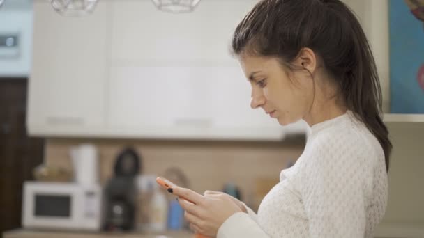 Brunette girl with white sweater using smartphone, texting and reading - Video, Çekim