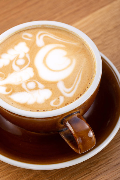 eine Tasse heißen Latte-Kaffee auf gealtertem braunem Holz, herzförmige Latte-Art, Kaffee-Liebhaber-Konzept. heißen Kaffee auf einem Holztisch. eine Tasse heißen Kaffee Latte, schöne Latte Art - Foto, Bild
