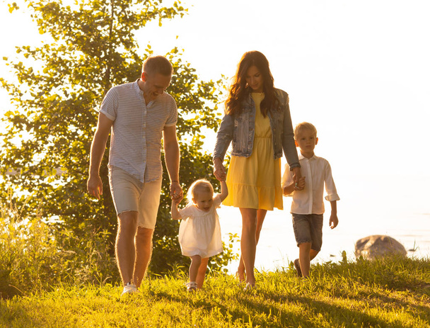 Happy family walking near the sea. Field and trees in countryside. Warm colors of sunset or sunrise. Loving parents and beautiful children. Love and parenthood concept. - Photo, Image