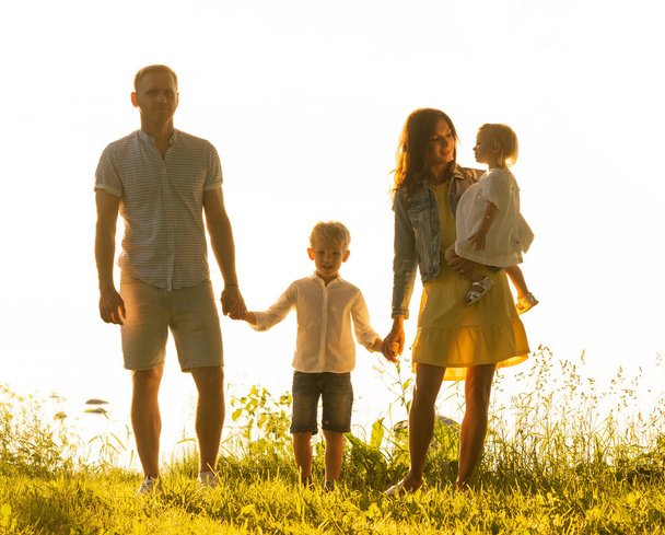 Happy family walking near the sea. Field and trees in countryside. Warm colors of sunset or sunrise. Loving parents and beautiful children. Love and parenthood concept. - Photo, Image