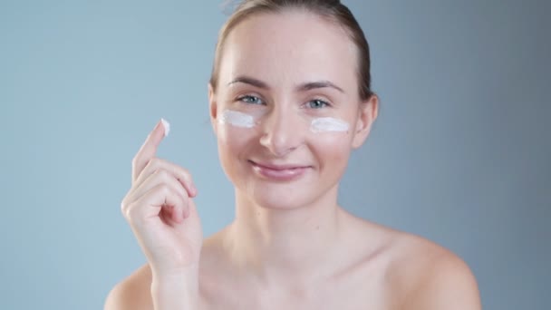 Young woman putting cream on her face isolated on background - Video