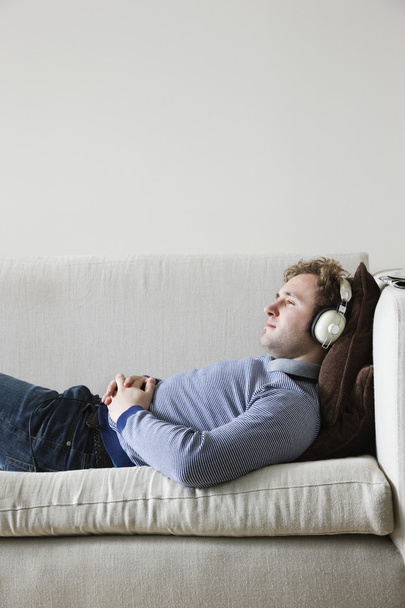 Man wearing headphones lying on sofa - Zdjęcie, obraz