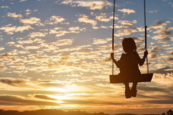 Silhouette des Kindes Mädchen ist Schaukel in Sonnenuntergang Hintergrund. - Foto, Bild