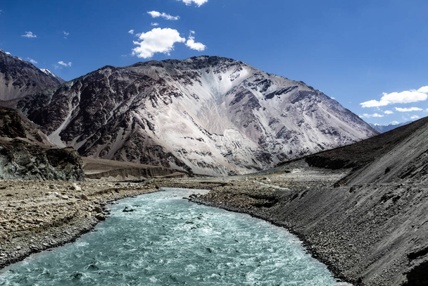 vivid landscape showing origin of a river at the base of a glacier with deep blue sky and snow capped barren himalayas of leh, kashmir, India - Photo, Image