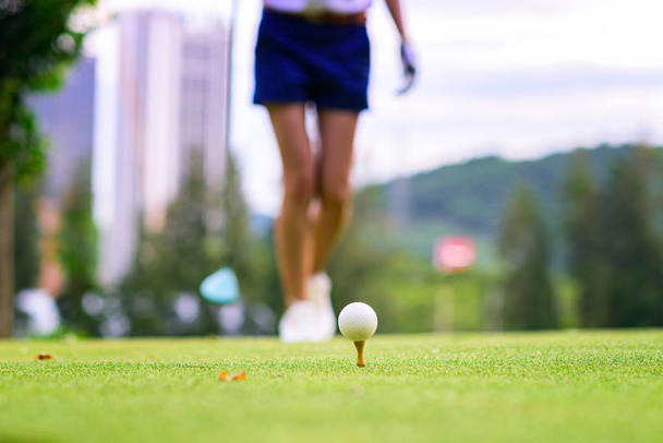 μπάλα του γκολφ που βρίσκεται στο ξύλινο Tee περιμένει για γυναίκα βόλτες για να χτυπήσει Tee- Off στο γήπεδο του γκολφ - Φωτογραφία, εικόνα