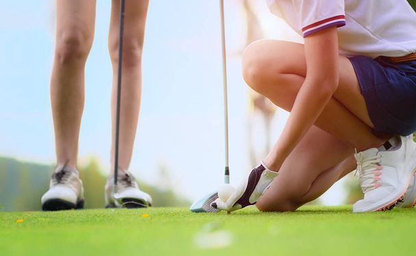 木製のティーに横たわってゴルフボールを保持若い女性のゴルフ選手の手,目的地のターゲットにボールを打つ準備と準備,背景で見て対戦相手やゴルフ仲間の仲間 - 写真・画像