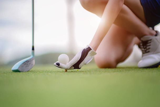 hand of young woman golf player holding golf ball push on wooden tee, ready to hit the ball to the destination target - Fotó, kép
