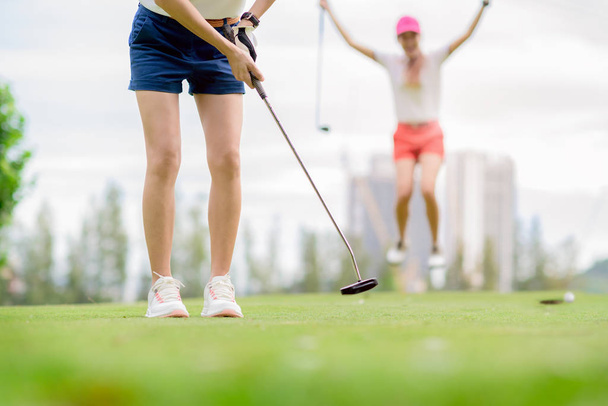 young woman golf player failed to putting golf ball into the hole on the green of the golf course, cheerfully and happiness on the failure of the opponent competitor in background  - Φωτογραφία, εικόνα