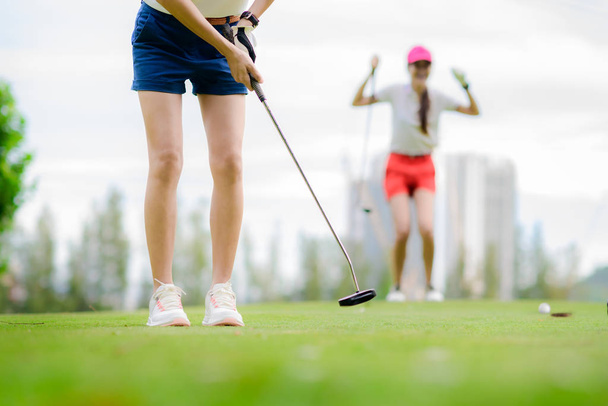 young woman golf player failed to putting golf ball into the hole on the green of the golf course, cheerfully and happiness on the failure of the opponent competitor in background  - Photo, Image
