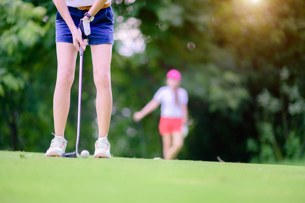 hand of young woman golf player holding putter to hit golf ball to the destination of golf hold on the green, competitpr or golfmate player watching in background - Foto, imagen
