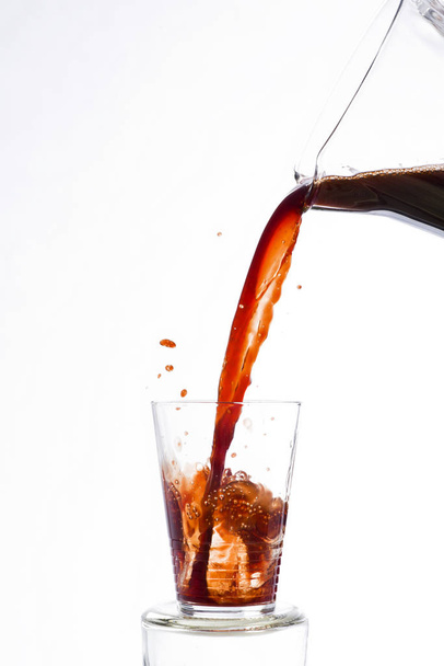 Drink, vigorously poured from a carafe, overflowing splashing from a glass, on a white background - Photo, Image