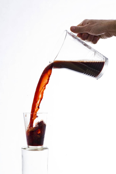 Drink, vigorously poured from a carafe, overflowing splashing from a glass, on a white background - Photo, Image