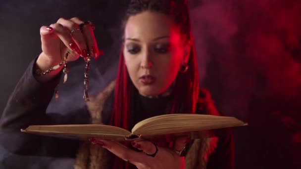 Bruja con libro de magia y amuleto contando hechizos en humo
 - Metraje, vídeo