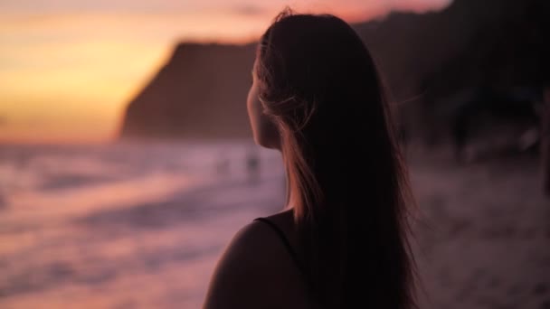 Puesta de sol sobre el océano. Joven mujer de pie en una playa su viento sopla en su pelo 4k
 - Metraje, vídeo