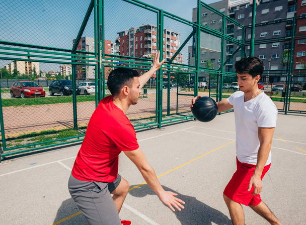 Two strong male basketball players play ball out doors fighting for a clean shot for three on a nice sunny day. - 写真・画像