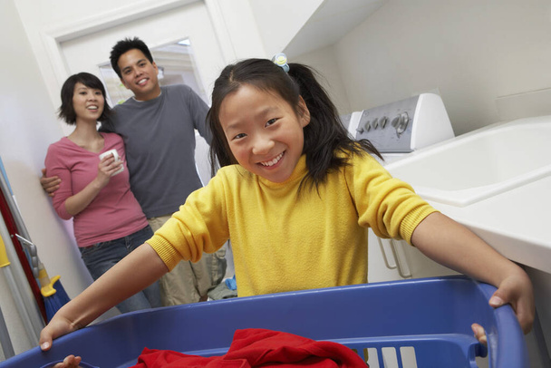 背景に両親と一緒に洗濯バスケットを保持幸せな十代の女の子の肖像画 - 写真・画像