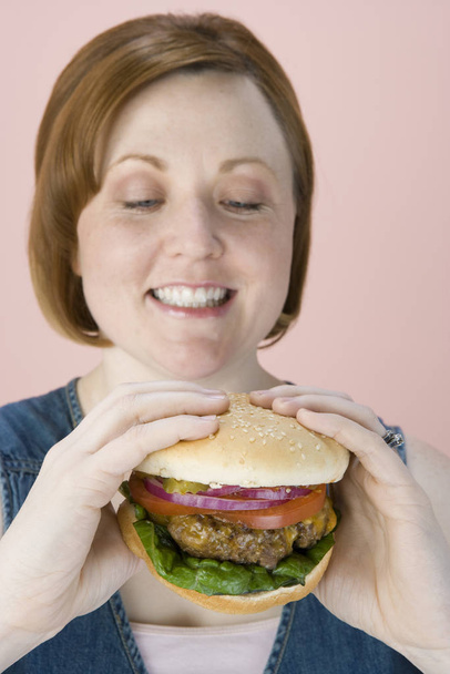 Happy beautiful woman looking at hamburger over pink background - Foto, afbeelding