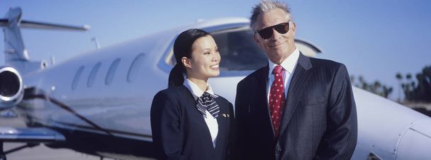 Portrait of senior businessman standing with beautiful stewardess in front of an aircraft - Fotó, kép