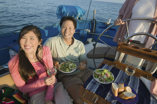Szczęśliwa para mając jedzenie z przyjacielem na kierownicy jachtu - Zdjęcie, obraz