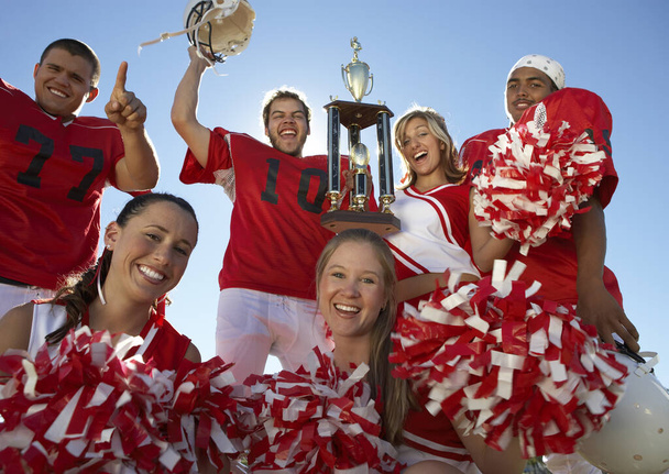 Portrait of excited players with cheerleaders holding trophy against clear sky - Foto, Imagem