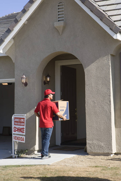 Worker delivering cardboard box into new house - Foto, imagen