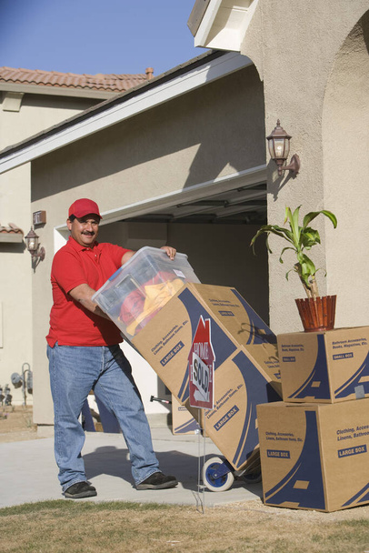 Worker unloading cardboard boxes in front of new house - Photo, Image