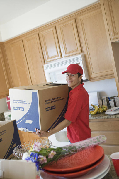 Portrait of a delivery man with cardboard box moving into new house - Photo, Image