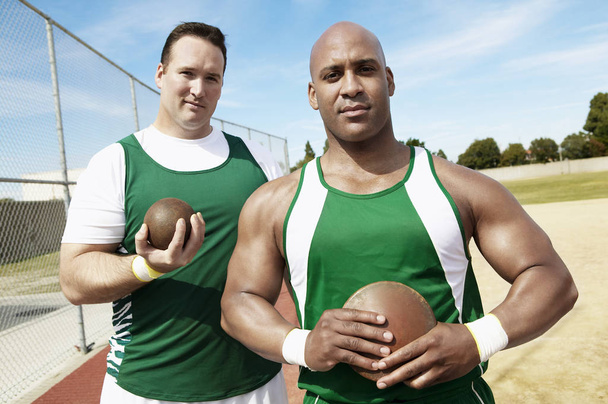 Portrait of shot putters holding shot put and discus on track and field - Фото, изображение