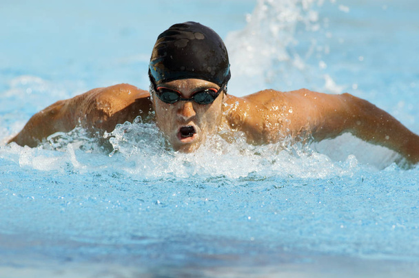 Competitive male swimmer in motion during swimming race - 写真・画像
