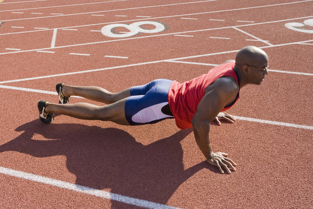 Full length of an African American male athlete makes pushups on a racetrack - Foto, Imagem
