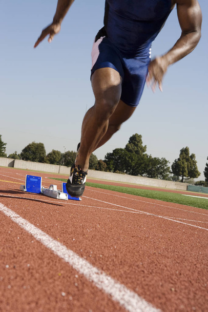 Low section of African American male runner beginning race from starting blocks - Photo, Image
