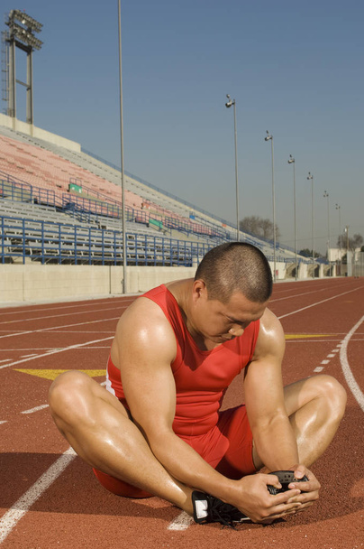 Full length of mature male athlete stretching on racetrack - Фото, изображение