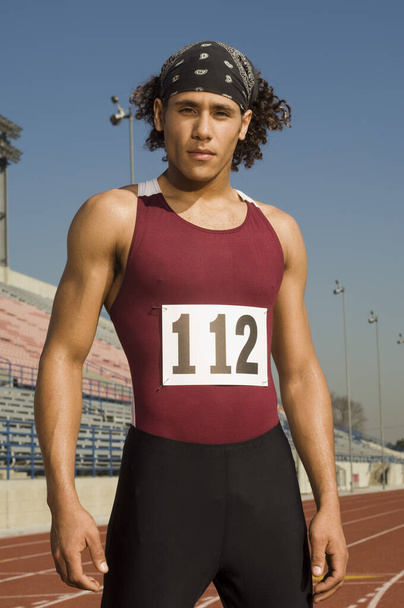 Portrait of confident young male athlete standing on racing track - Фото, изображение