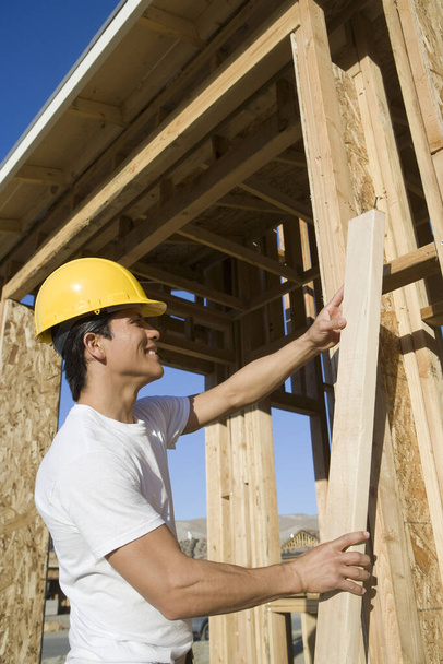 Middle aged construction worker holding a wooden beam at construction site - Photo, Image