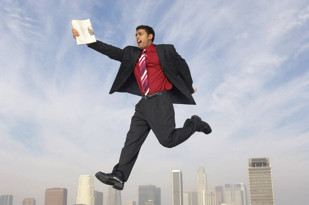 Full length of mixed race businessman running in midair with newspaper - Fotó, kép