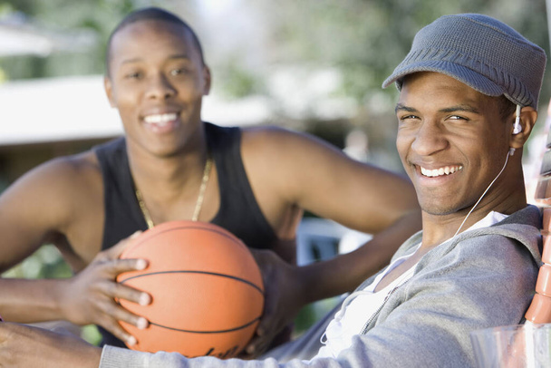 Portrait of a happy African American man on deck chair with friend holding basketball - Φωτογραφία, εικόνα