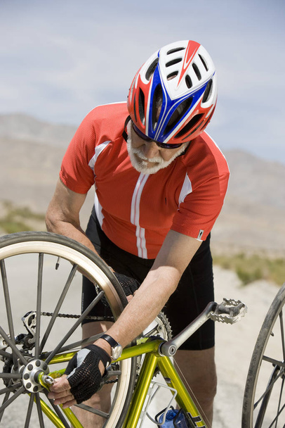 Senior male cyclist repairing cycle - Valokuva, kuva