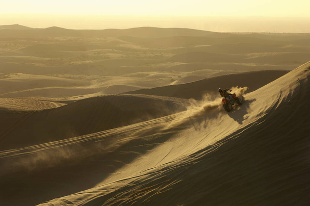 Man riding quad bike in desert at sunset - Фото, изображение