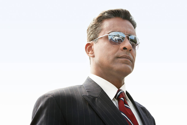 Confident mature businessman in sunglasses looking at helicopter against clear sky - Foto, afbeelding