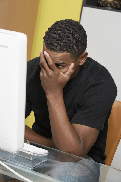 Tensed young African American man looking at desktop PC - Photo, image