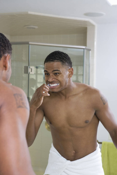 Young African American man brushing teeth in front of mirror - Fotografie, Obrázek